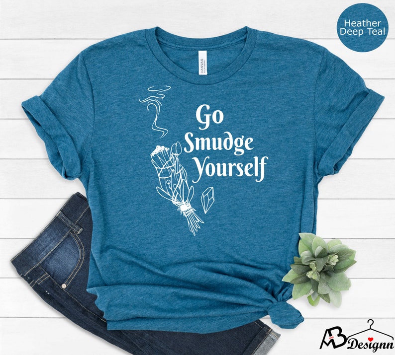 K&ouml;nnte beinhalten: Ein blaues T-Shirt mit dem Text "Go Smudge Yourself" in Wei&szlig;. Das Shirt zeigt eine wei&szlig;e Illustration eines R&auml;ucherstabs mit aufsteigendem Rauch.