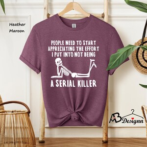 May include: A heather maroon t-shirt with a white skeleton graphic and the text "PEOPLE NEED TO START APPRECIATING THE EFFORT I PUT INTO NOT BEING A SERIAL KILLER".
