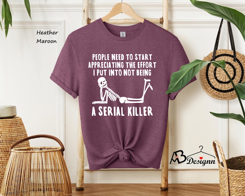 May include: A heather maroon t-shirt with a white skeleton graphic and the text "PEOPLE NEED TO START APPRECIATING THE EFFORT I PUT INTO NOT BEING A SERIAL KILLER".