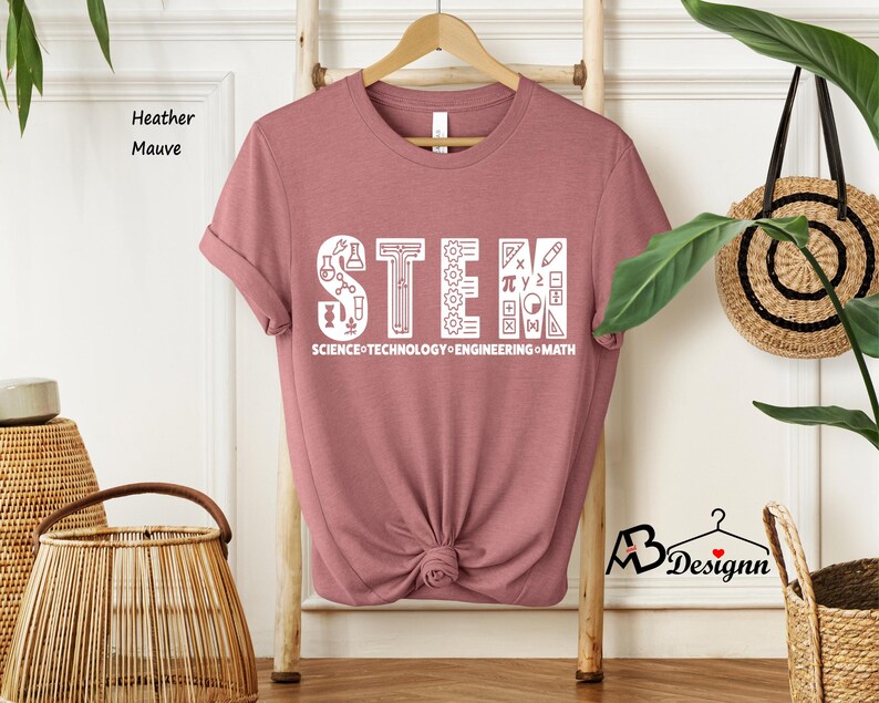 May include: A heather mauve t-shirt with the word "STEM" in white letters. The letters are made up of science, technology, engineering, and math symbols. The text "SCIENCE-TECHNOLOGY-ENGINEERING-MATH" is printed below the word STEM.