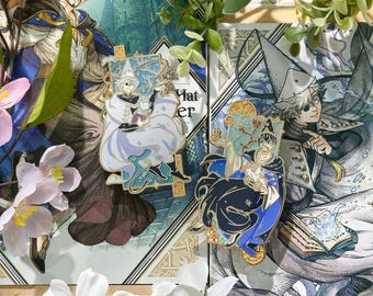 May include: Two enamel pins featuring anime-style illustrations of characters in wizard attire. One pin has a white and light blue color scheme, while the other is dark blue and gold. The pins are set against a backdrop of illustrated artwork and white flowers.