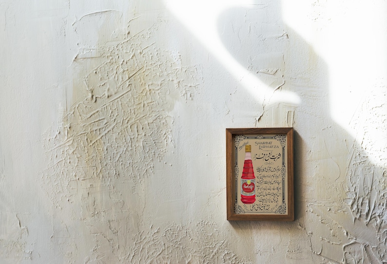 May include: A framed vintage advertisement for "Sharbat El-Rubbarda" featuring a red bottle with Arabic text. The advertisement is in a wooden frame with a white background.