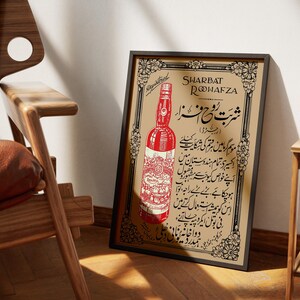 May include: A vintage framed poster advertising Sharbat Rooh Afza, a popular Indian beverage. The poster features a red bottle with a gold label and Urdu text.