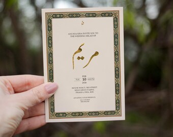 May include: A cream-colored wedding invitation with gold calligraphy and a decorative green and gold border. The invitation includes the names of the couple, the date, time, and location of the wedding.