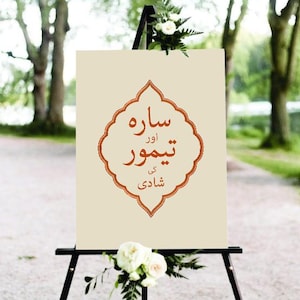 Op de afbeelding: Een wit bord met een rode rand en Arabische tekst die "Sawre Awwr Teshwor Ki Shaadi" luidt, op een ezel voor een groene achtergrond.