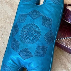 Peut inclure: Un coussin en cuir turquoise de forme originale, orné de motifs géométriques en relief. Le design comprend une étoile centrale et des motifs en losange, alliant esthétisme et confort.