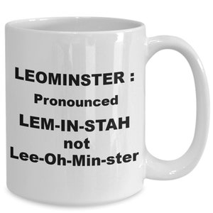 Może przedstawiać: Biały kubek ceramiczny z czarnym tekstem, który brzmi "LEOMINSTER: Wymawiane LEM-IN-STAH, a nie Lee-Oh-Min-ster"