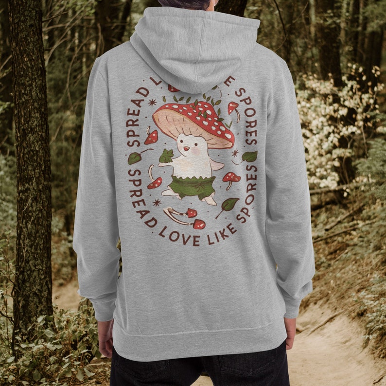 May include: A gray hooded sweatshirt with a graphic print of a mushroom character. The text around the character reads "Spread love like spores".