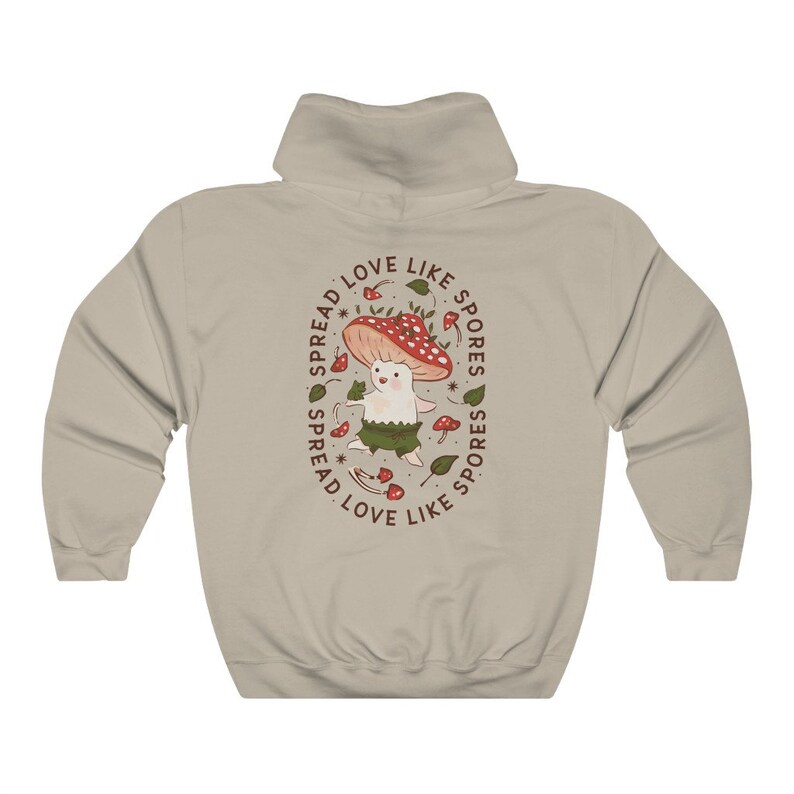 The back of a long-sleeved sand color hoodie. It has an art imprint of the colorful mushroom Amanita Muscaria in cartoon form and the words Spread Love Like Spores around the art.