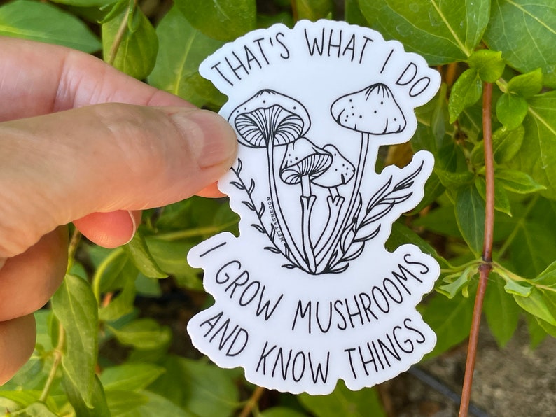 A premium 3 inch by 2 inch die-cut vinyl sticker. The sticker graphic is a black and white cluster of mushrooms with black text. The text says That's What I Do. I Grow Mushrooms And Know Things. Our stickers are waterproof/UV resistant.