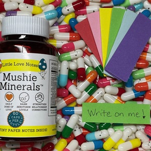 May include: A brown bottle of "Mushie Minerals" supplements with colorful capsules scattered around. The bottle has a white lid and a label with text and mushroom illustrations. A stack of colorful paper notes and a green note that says "Write on me!" are also present.