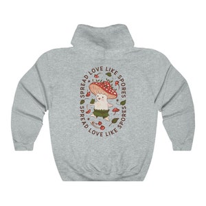 The back of a long-sleeved ash color hoodie. It has an art imprint of the colorful mushroom Amanita Muscaria in cartoon form and the words Spread Love Like Spores around the art.