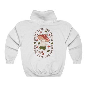 The back of a long-sleeved white color hoodie. It has an art imprint of the colorful mushroom Amanita Muscaria in cartoon form and the words Spread Love Like Spores around the art.