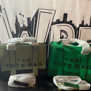 May include: Two tote bags, one green and one olive green, with black straps and the text "THE TOTE BAG" printed on the front.