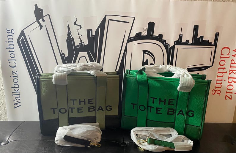 May include: Two tote bags, one green and one olive green, with black straps and the text "THE TOTE BAG" printed on the front.