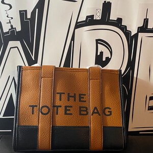 May include: A brown and black tote bag with the text "THE TOTE BAG" printed on the front.