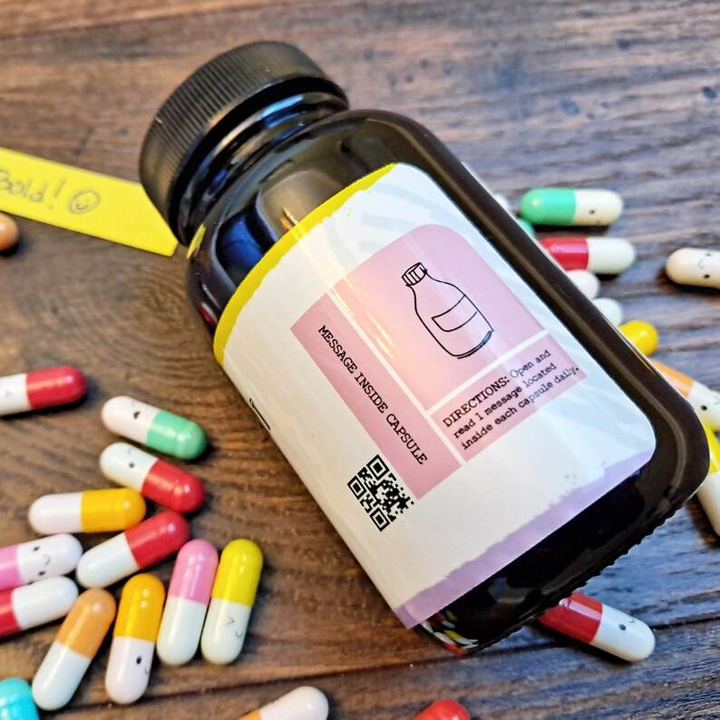 May include: A black bottle with a pink and white label that says "MESSAGE INSIDE CAPSULE" and "DIRECTIONS: Open and read 1 message located inside each capsule daily." The bottle is surrounded by small colorful capsules with smiley faces on them.