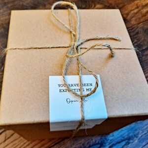 May include: A brown cardboard box tied with twine and a white tag that says "You have been expecting me. Open me."