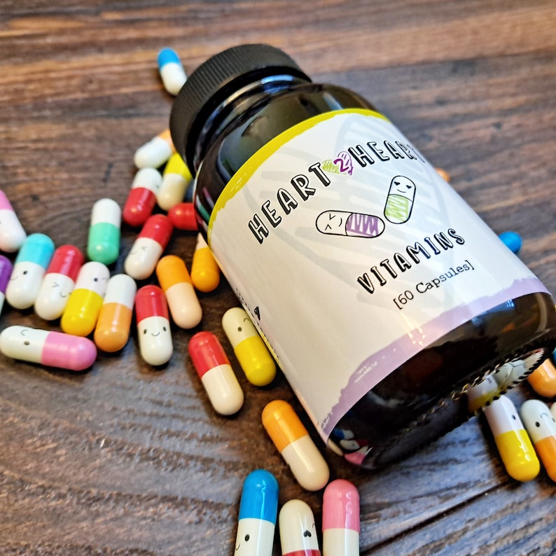 May include: A bottle of Heart 2 Heart Vitamins with a purple, yellow, and white label. The label has a cartoon heart with two pills inside and the text "Heart 2 Heart Vitamins (60 Capsules)". The bottle is surrounded by colorful capsules with smiley faces.