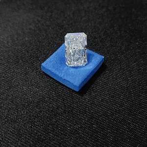 Könnte beinhalten: Ein klarer, rechteckiger, facettierter Edelstein auf einem blauen Samtkissen.