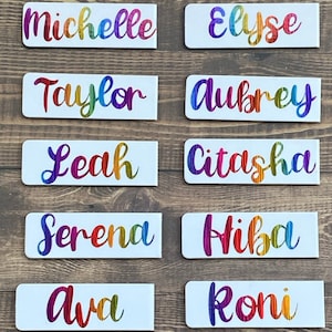 May include: Ten white rectangular name tags with rainbow lettering. The names on the tags are Michelle, Elyse, Taylor, Aubrey, Leah, Citasha, Serena, Hiba, Ava, and Roni.