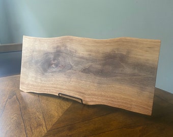 Könnte beinhalten: Ein großes, natürliches Holz-Serviertablett mit welligem Rand. Das Tablett hat eine hellbraune Farbe mit dunkleren braunen Holzmaserungen.