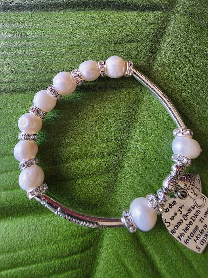 Peut inclure: Un bracelet de perles avec des d&eacute;tails argent&eacute;s et un charm en forme de c&oelig;ur. Le bracelet pr&eacute;sente de grosses perles blanc cass&eacute; s&eacute;par&eacute;es par des entretoises argent&eacute;es avec des cristaux clairs. Un charm en forme de c&oelig;ur avec du texte grav&eacute; est suspendu.