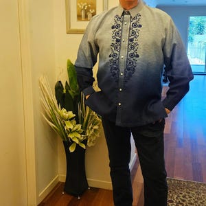 May include: A long-sleeved button-down shirt featuring an ombre effect that transitions from light blue at the shoulders to dark blue at the hem. The shirt includes a vertical panel of dark blue floral embroidery along the center front placket.