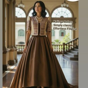 May include: A woman wearing a brown formal dress with a matching bolero jacket. The bolero is beige with brown stripes. The dress has a full skirt and is floor-length. The image includes text that says "Kalinga Bolero Simply classy Effortless Filipina".