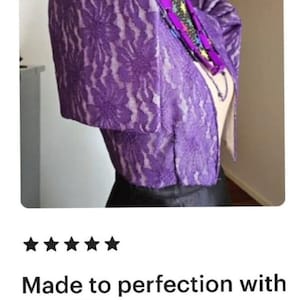 May include: A vibrant purple lace bolero jacket featuring structured, puffed butterfly sleeves and a floral pattern. The garment is displayed on a mannequin, paired with a dark necklace featuring purple rectangular beads and a star-patterned collar.