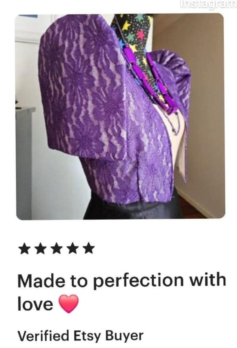 May include: A vibrant purple lace bolero jacket featuring structured, puffed butterfly sleeves and a floral pattern. The garment is displayed on a mannequin, paired with a dark necklace featuring purple rectangular beads and a star-patterned collar.