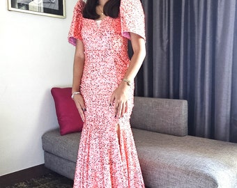 May include: A coral-colored, sequined formal gown with a mermaid silhouette. The dress features short, puffed sleeves and a thigh-high slit. The gown is floor-length and appears to be made of a shimmering fabric, suitable for special occasions.