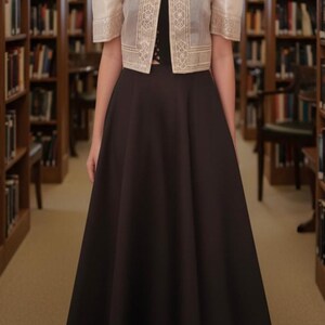 May include: A black floor-length skirt paired with a black top and a cream-colored bolero jacket. The jacket features structured butterfly sleeves, a high collar, and intricate gold embroidery along the front panels and sleeve hems.