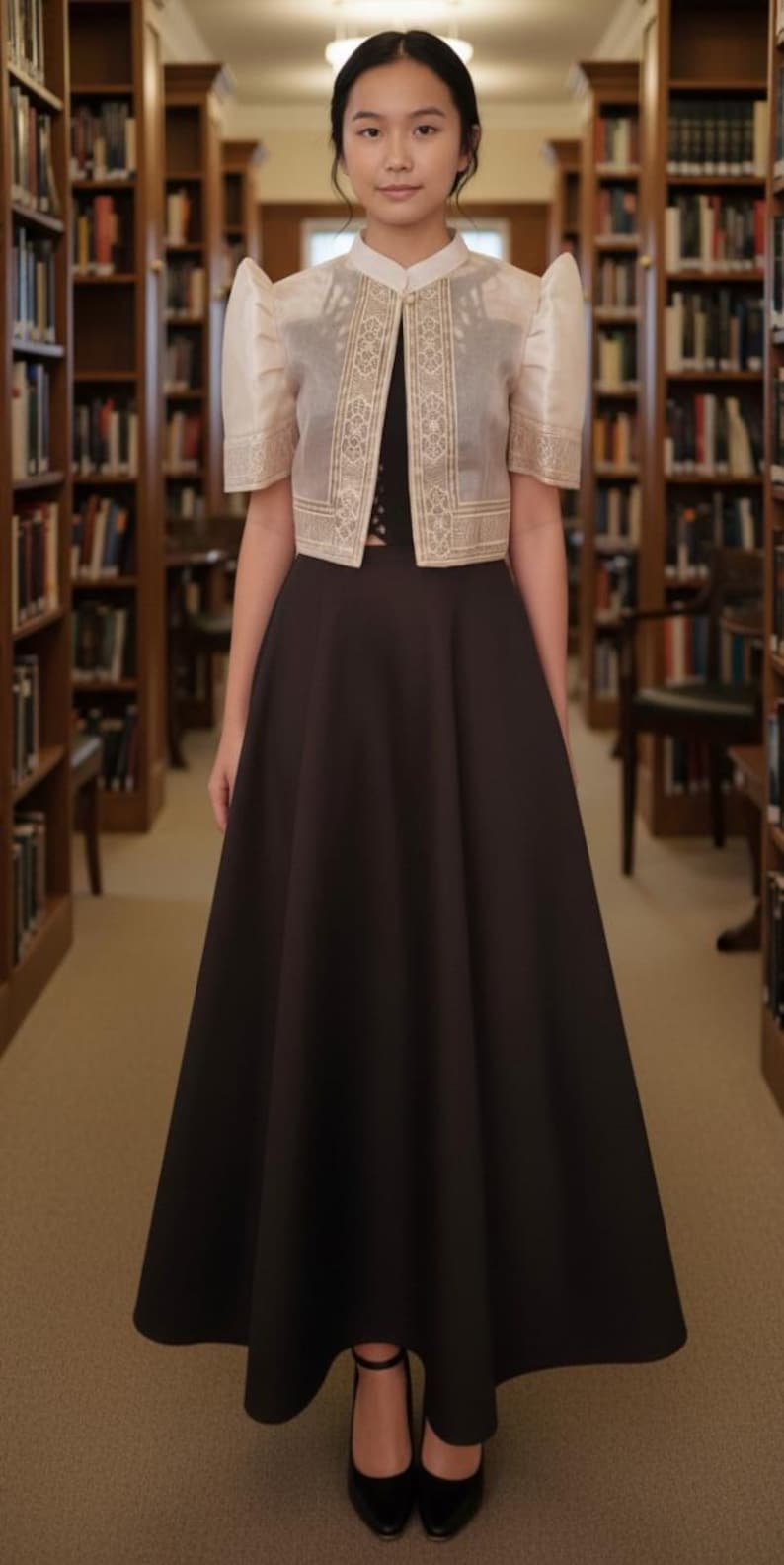 May include: A black floor-length skirt paired with a black top and a cream-colored bolero jacket. The jacket features structured butterfly sleeves, a high collar, and intricate gold embroidery along the front panels and sleeve hems.
