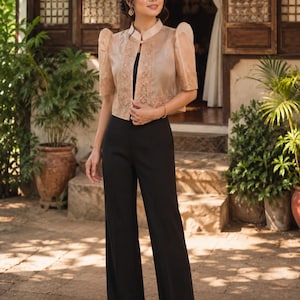 May include: A beige organza bolero jacket with short puff sleeves, a mandarin collar, and intricate embroidery along the front edges, paired with high-waisted black wide-leg trousers and a simple black top underneath the sheer jacket.