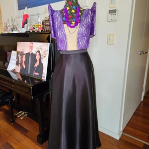 May include: A two-piece ensemble featuring a purple lace bolero with structured butterfly sleeves and a solid black floor-length satin skirt. The outfit is displayed on a mannequin wearing a black necklace and a colorful star-patterned collar.