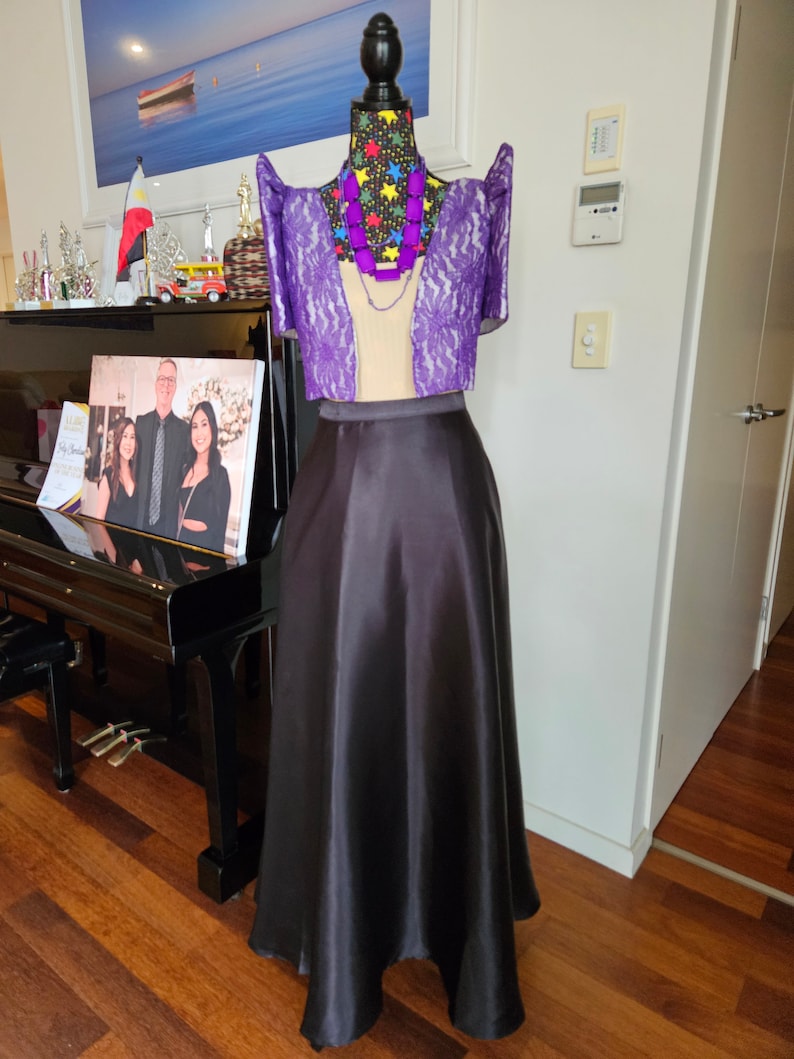 May include: A two-piece ensemble featuring a purple lace bolero with structured butterfly sleeves and a solid black floor-length satin skirt. The outfit is displayed on a mannequin wearing a black necklace and a colorful star-patterned collar.
