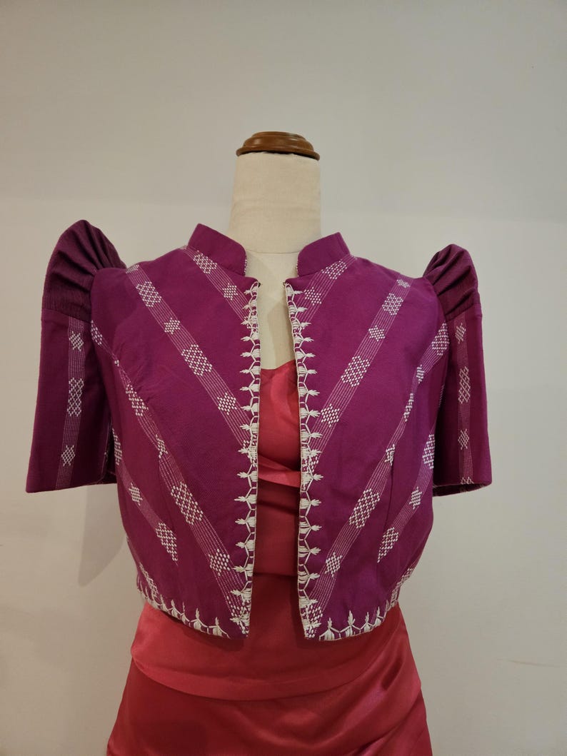 May include: A vibrant purple bolero jacket with white embroidered details and short, puffed sleeves. The jacket features a mandarin collar and a tailored fit. The design includes diagonal white embroidered stripes. The jacket is displayed on a mannequin.