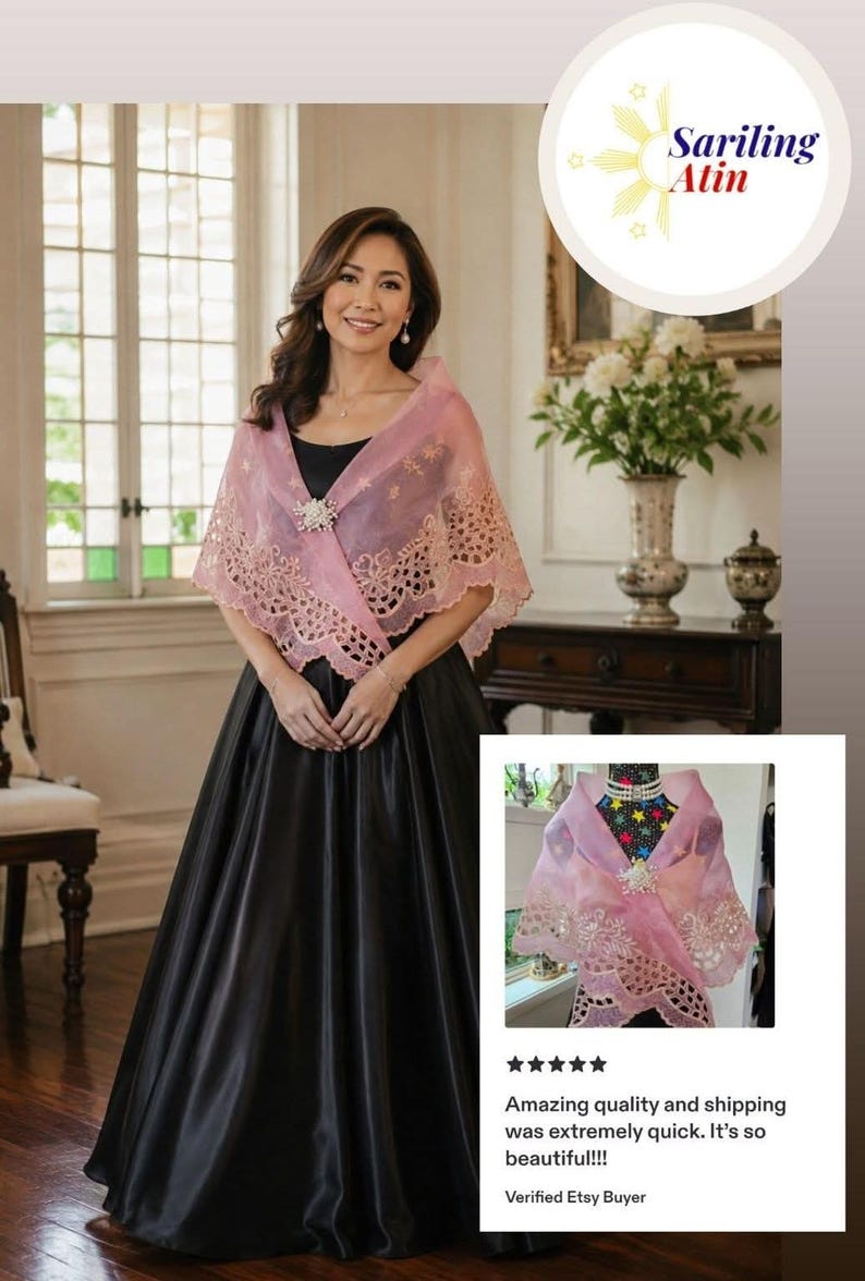 May include: A sheer, light pink shawl featuring intricate floral embroidery along the scalloped edges and a central decorative brooch. The shawl is draped over a black sleeveless gown, showcasing a delicate, translucent fabric with detailed stitching.