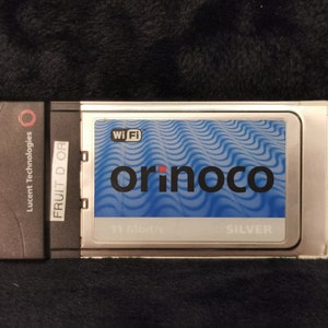 May include: A silver and black wireless network card with the text "Wi-Fi orinoco SILVER 11 Mbit/s" on it. The card is made by Lucent Technologies.
