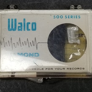 May include: A close-up of a clear plastic case containing a Walco 500 Series Diamond needle for records. The case has a white background with blue text and a graphic of a sound wave.