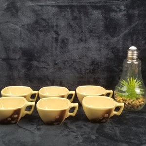 May include: Set of six brown and beige ceramic coffee cups with a brown and white design. The cups have square-shaped bodies and rounded handles.