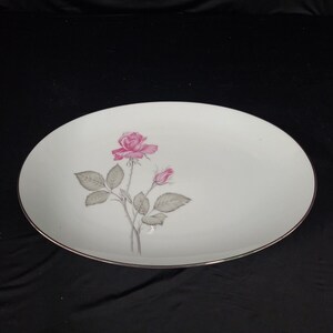 Puede incluir: Plato ovalado blanco para servir con borde dorado y una sola rosa rosa con hojas verdes y un capullo.
