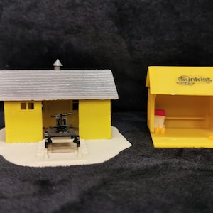 May include: Two yellow miniature buildings, one with a gray roof and a black loading dock, the other with the text "Sunkist" on the roof.