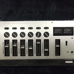 May include: A silver Sony MX-14 8-channel stereo microphone mixer with multiple knobs and sliders. The mixer has two VU meters and a headphone jack.