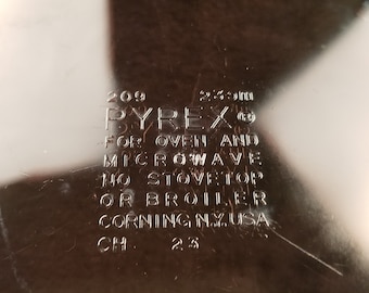 Puede incluir: Primer plano de una fuente para hornear de la marca Pyrex con el texto "209 2.3L Pyrex para horno y microondas no para estufa o parrilla Corning NY. USA CH 2.3" grabado en la parte inferior.