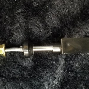 Könnte beinhalten: Ein schwarzer Metall-Kippschalter mit einer silbernen Schraube und Mutter. Der Schalter ist auf einer silbernen Stange montiert.