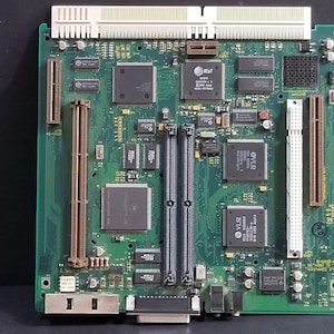 Op de afbeelding: Een groene printplaat met diverse elektronische componenten, waaronder chips, connectoren en slots. De kaart heeft een rechthoekige vorm en beschikt over meerdere geïntegreerde circuits met tekstlabels. Het algehele ontwerp suggereert een computercomponent.