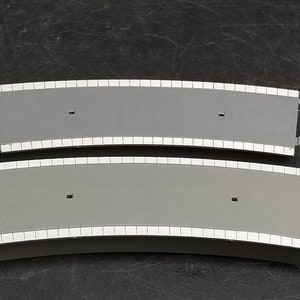 May include: Two gray plastic curved track pieces with white edging. The pieces are designed to connect to create a curved track for a model train set.