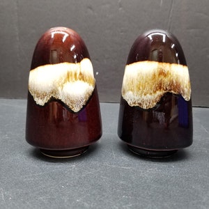 Può includere: Un paio di saliere e pepiere in ceramica marrone e bianca a forma di cono arrotondato.